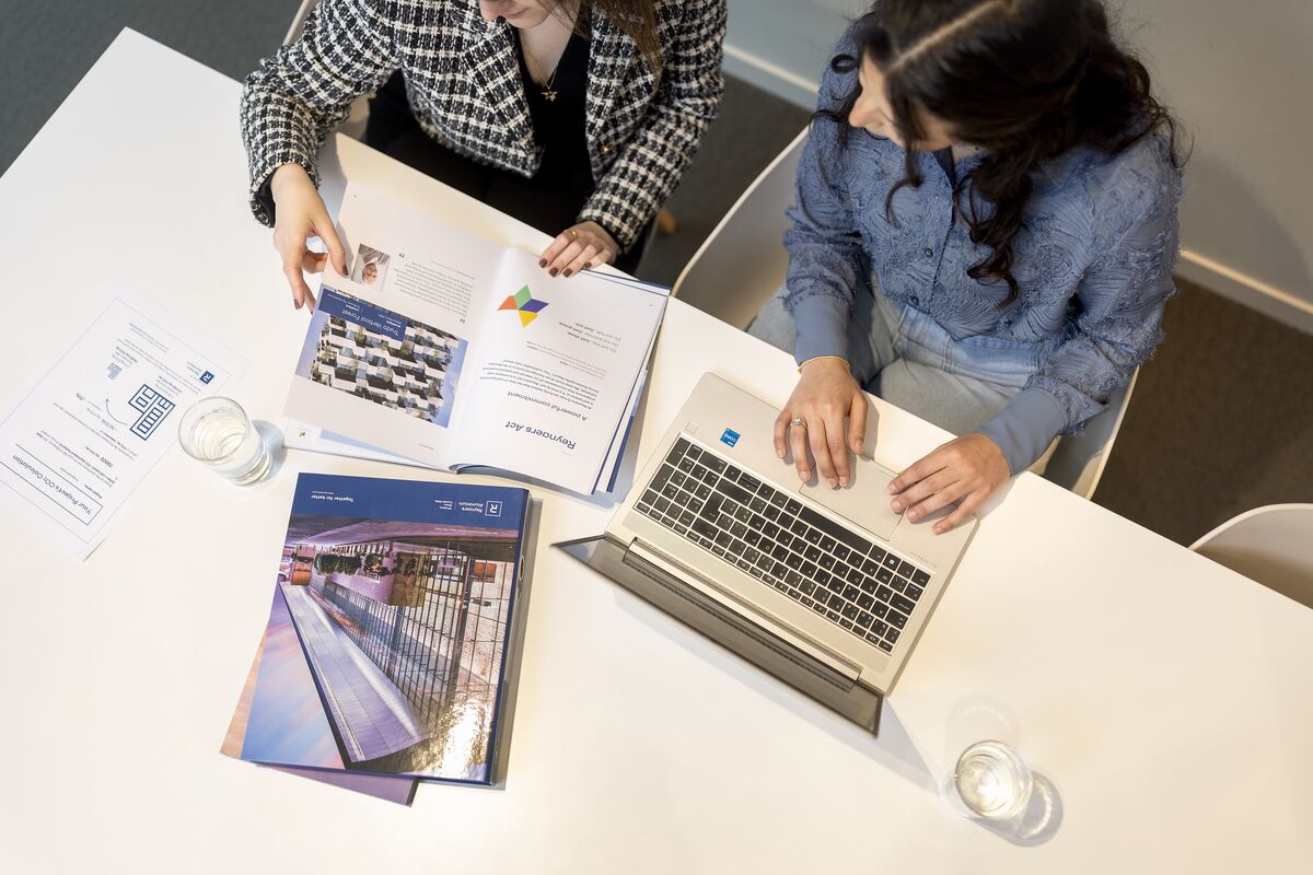 Pohled shora na stůl s papíry, notebookem a pořadači.