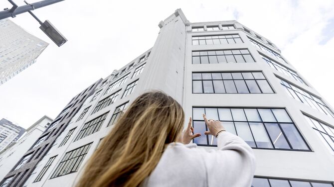 Žena zvedá ruce směrem k bílé středně vysoké budově se spoustou oken.