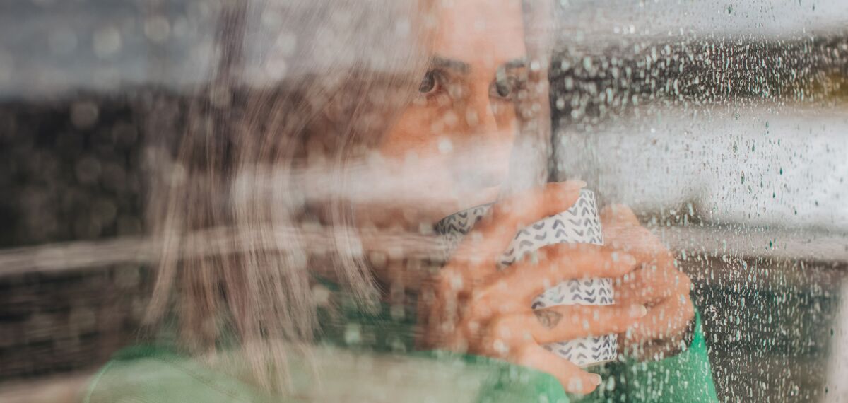 Woman drinking coffee behind glass window on a rainy day.