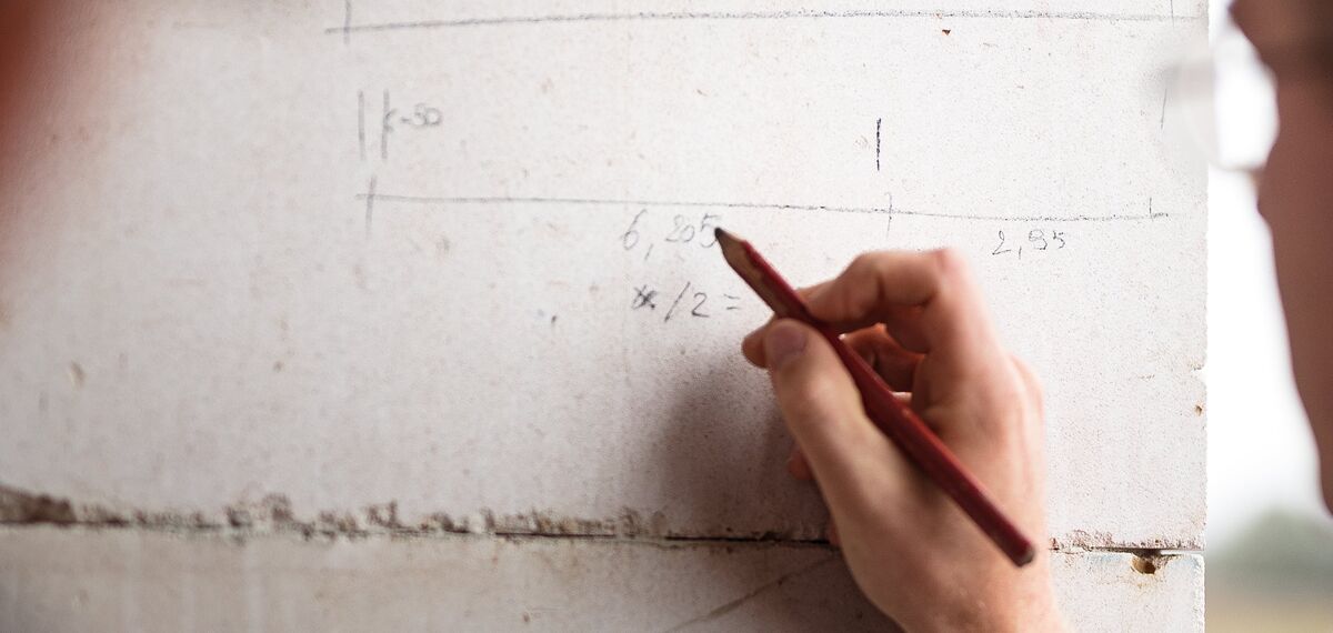 Muž píše tužkou na betonovou zeď staveniště.