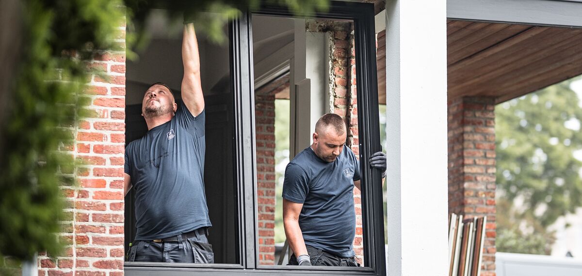 Dva montéři umisťují nové hliníkové profily do renovovaného domu.