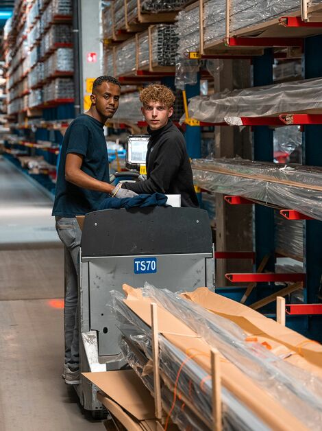 Two Reynaers co-workers transporting aluminium profiles in the warehouse.