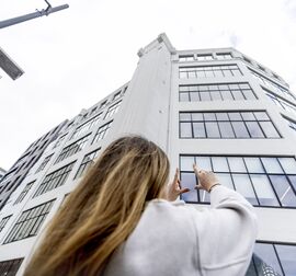 blondýnka před bílou výškovou budovou ve městě