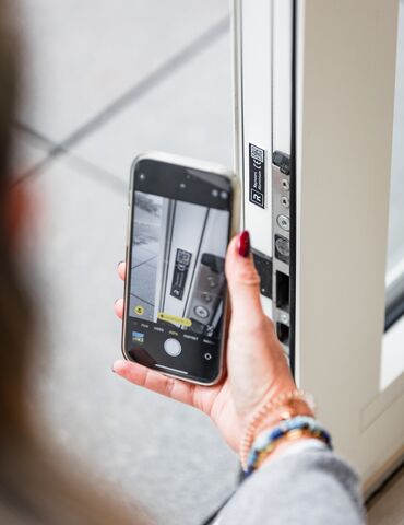 Ruka držící smartphone v blízkosti QR kódu na bílém okenním profilu.